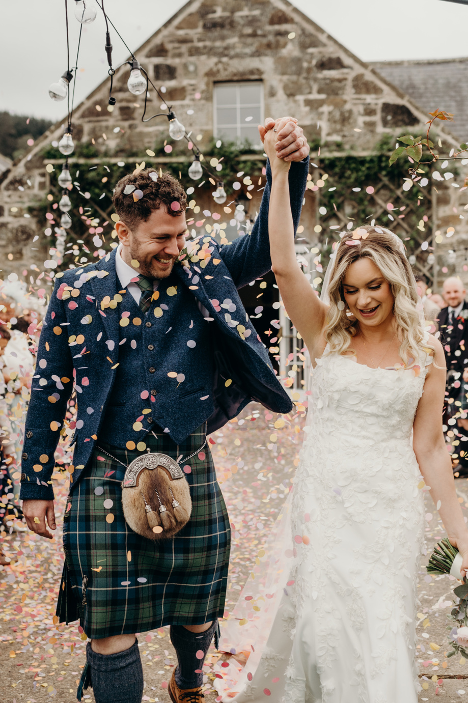 Bride and groom put arms in air walking through confetti shot